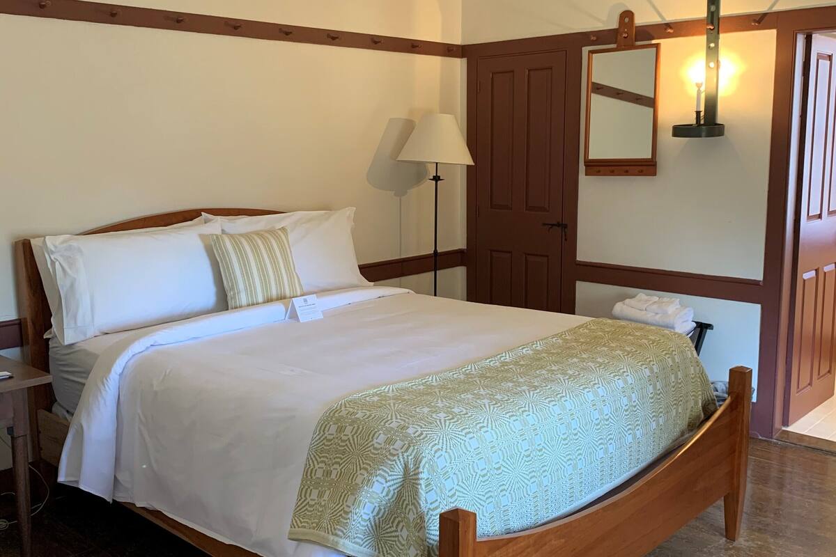 A neatly made bed with a patterned bedspread and pillows, a bedside lamp, and a wooden nightstand.