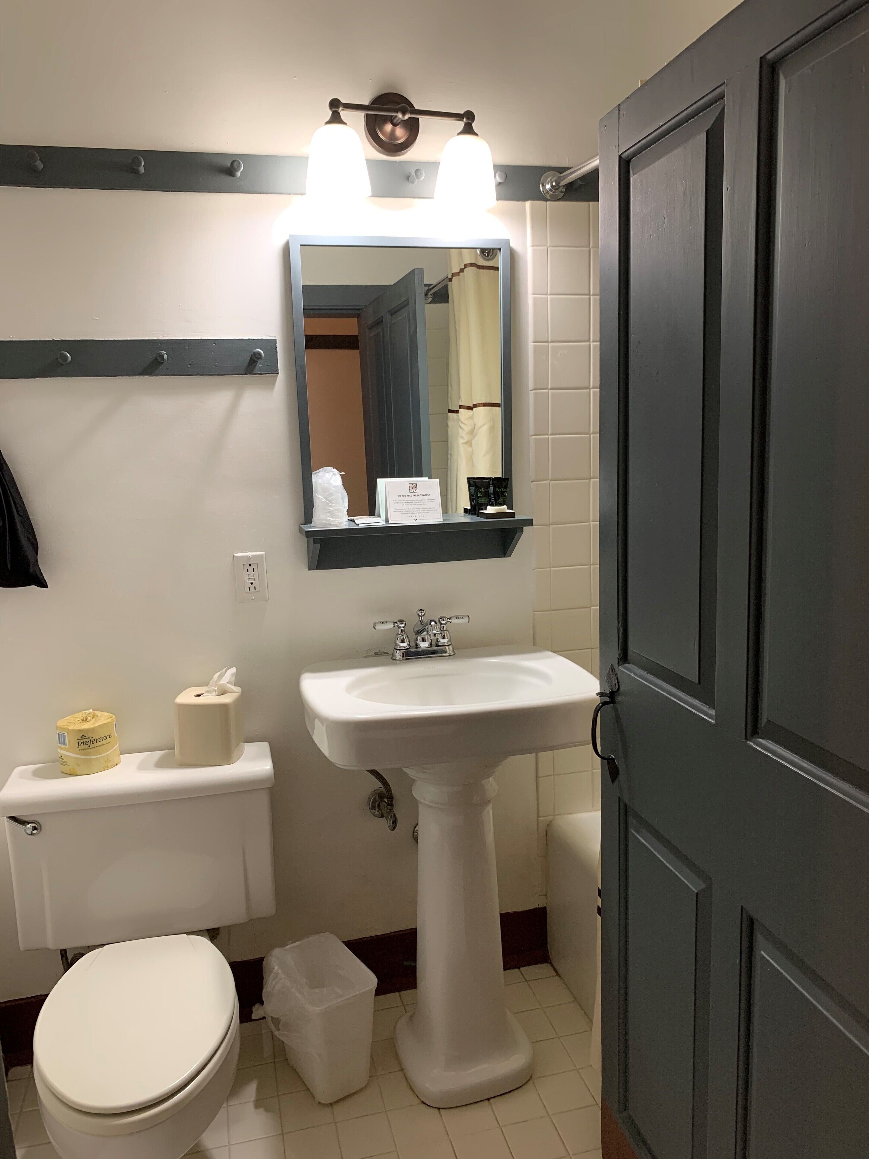 Un baño con un lavamanos blanco, un espejo encima, un inodoro y un cubo de basura.
