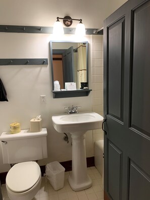 Une salle de bain avec un lavabo blanc, un miroir au-dessus, des toilettes et une poubelle.