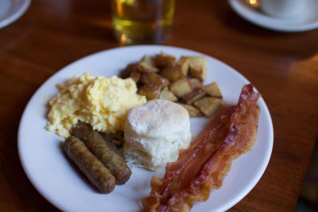 Un plato con huevos revueltos, salchichas, un bizcocho y tocino.