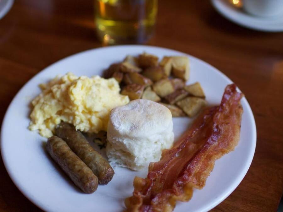 Un plato con huevos revueltos, salchichas, un bizcocho y tocino.