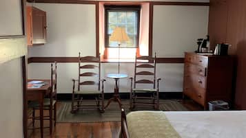 A room with a bed, wooden chairs, a small table, a lamp, a dresser, and a window with a view.