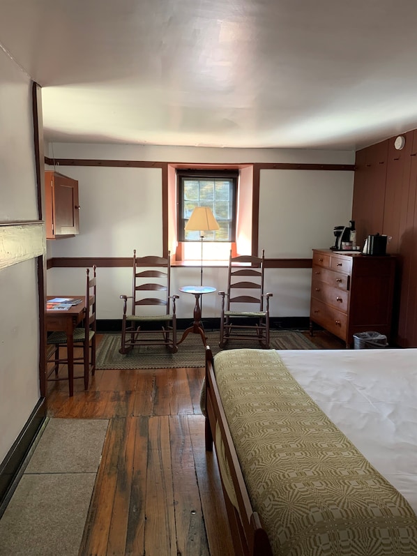 A room with a bed, wooden chairs, a small table, a lamp, a dresser, and a window with a view.