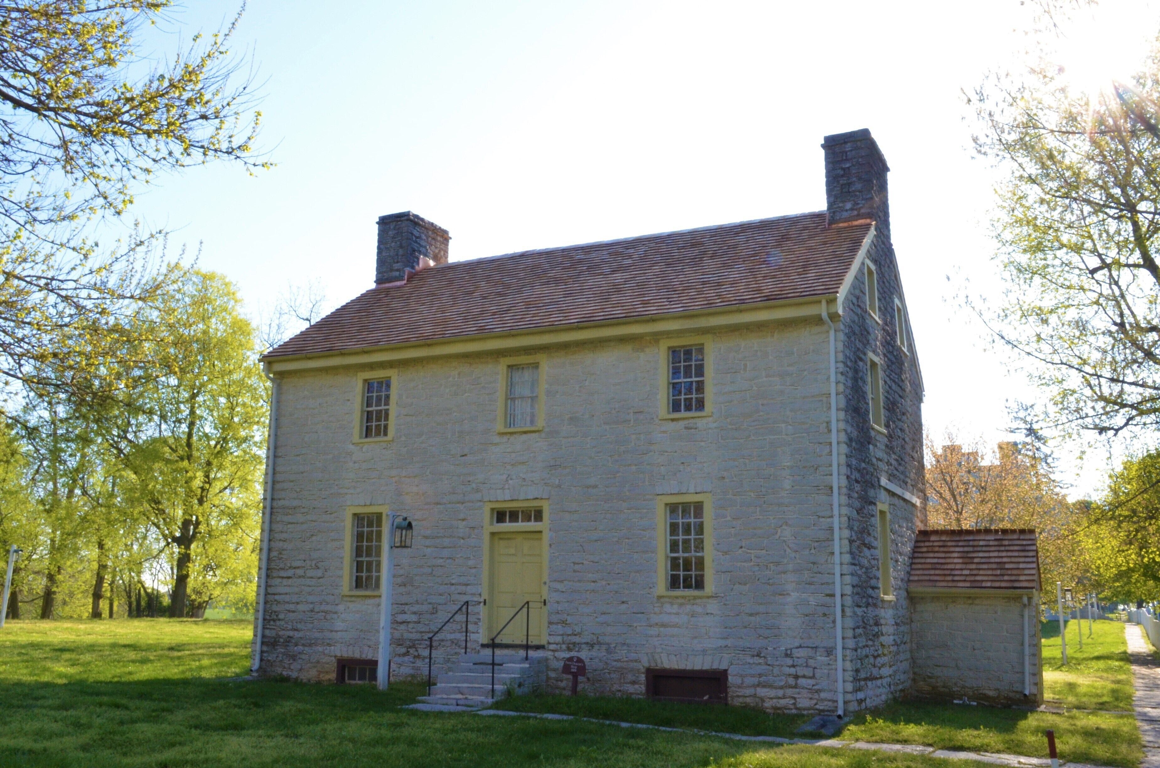 A two-story stone building with a yellow door and windows, surrounded by trees.