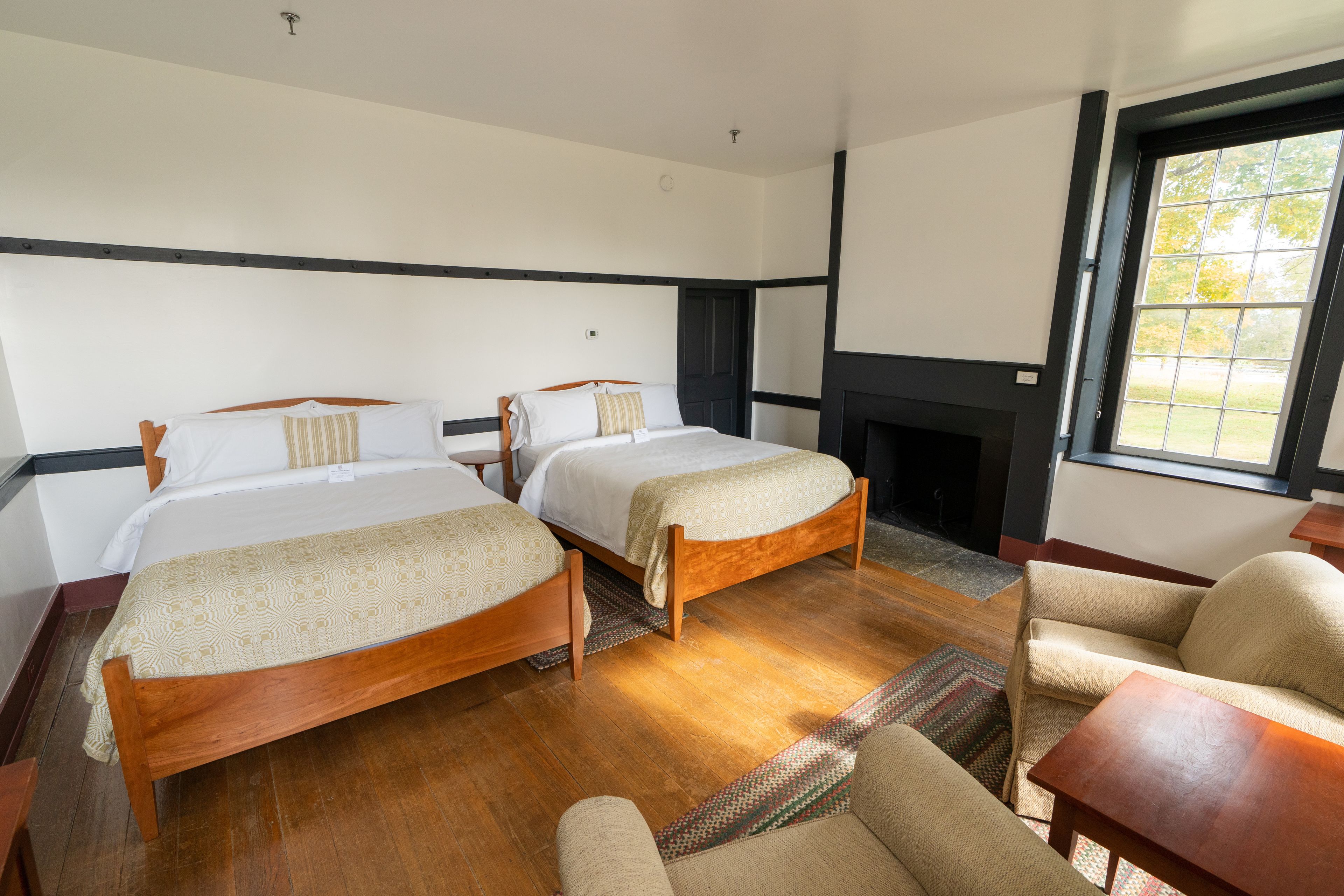 A hotel room with two wooden beds, a sofa, a small table, and a fireplace.