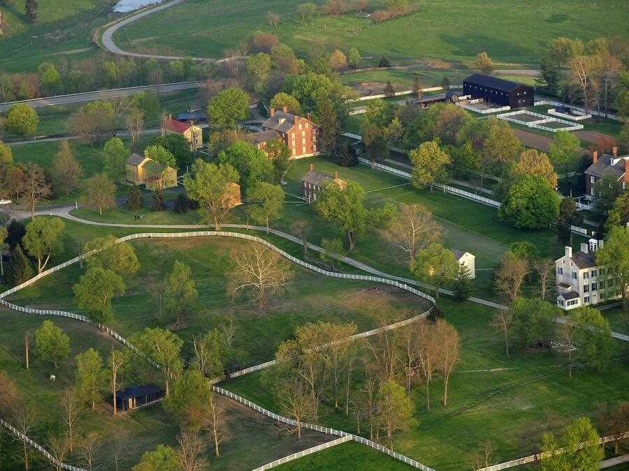 A rural landscape with a winding road, several buildings, and fenced areas.