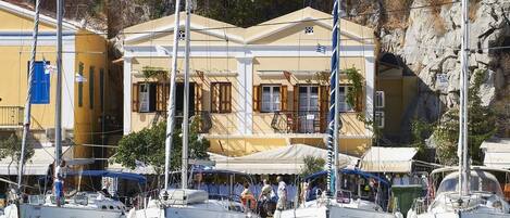 Eine Marina mit mehreren angestaubten Segelbooten. Ein Gebäude mit gelber Fassade und weißem Zierrat, und Personen sind am Steg versammelt.