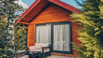 A wooden cabin with a large sliding glass door, a small porch with a bench, and a gravel pathway.