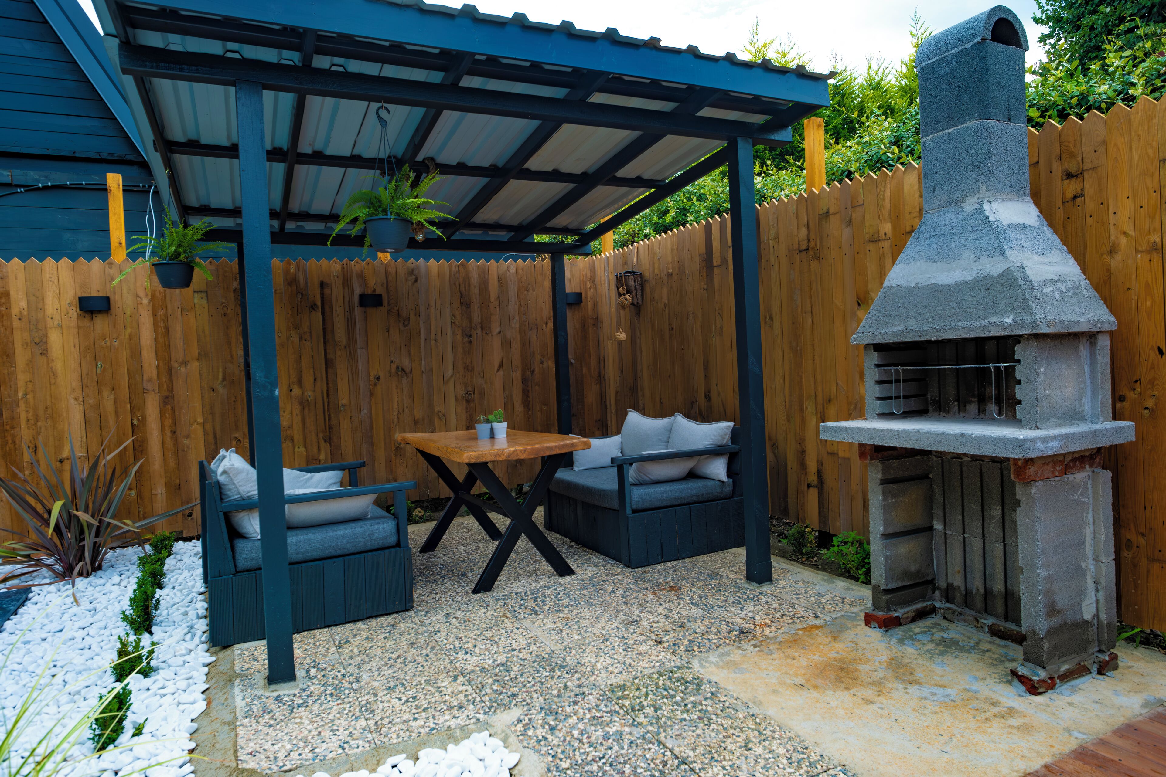 Un patio con una zona de estar cubierta, una parrilla y una valla de madera.