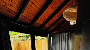 Ein Schlafzimmer mit Holzboden, einem großen Fenster, einem Bett, einem kleinen Tisch und Blick auf einen Holzzaun sowie ein Whirlpool im Freien.