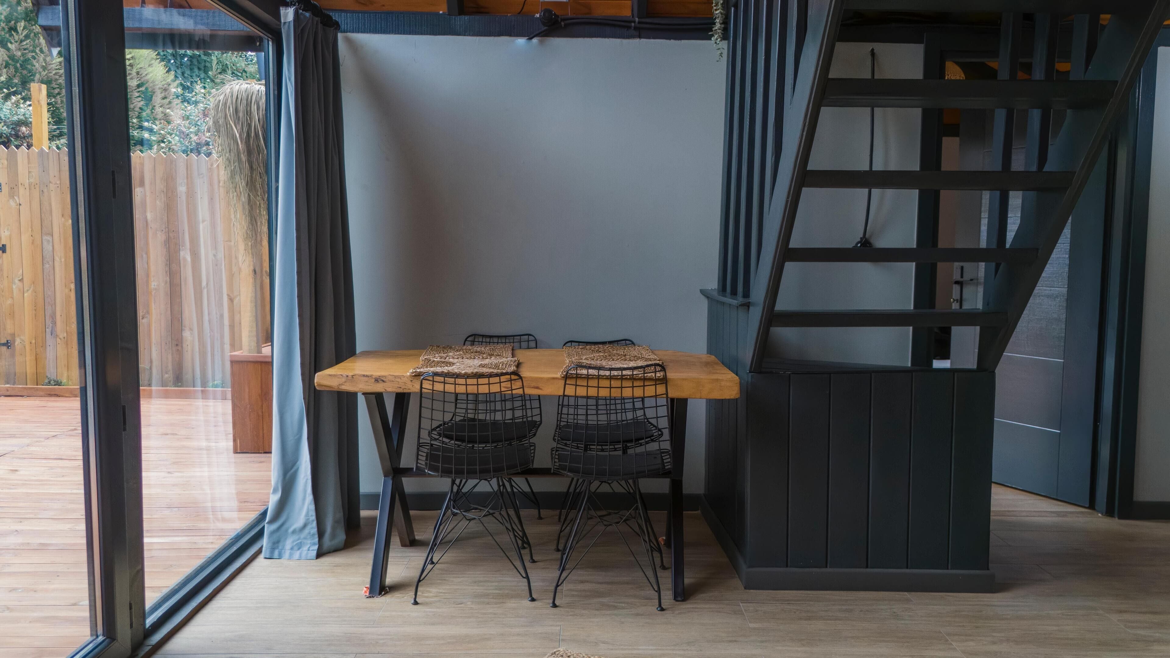 A dining area with a wooden table and black wire chairs, a staircase, and a view of a wooden deck outside.