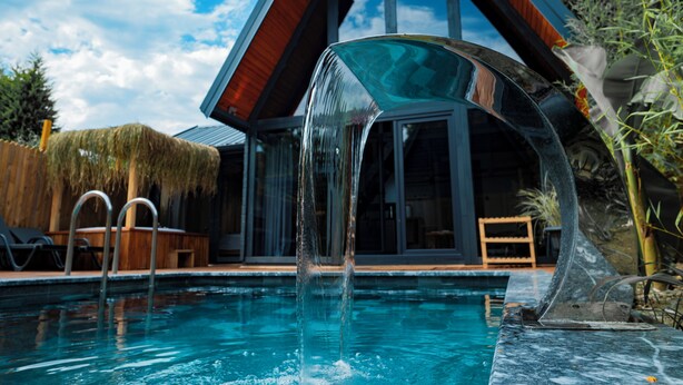 Ein modernes Haus mit Pool, einem Wasserspiel aus Glas und einer Holzterrasse.