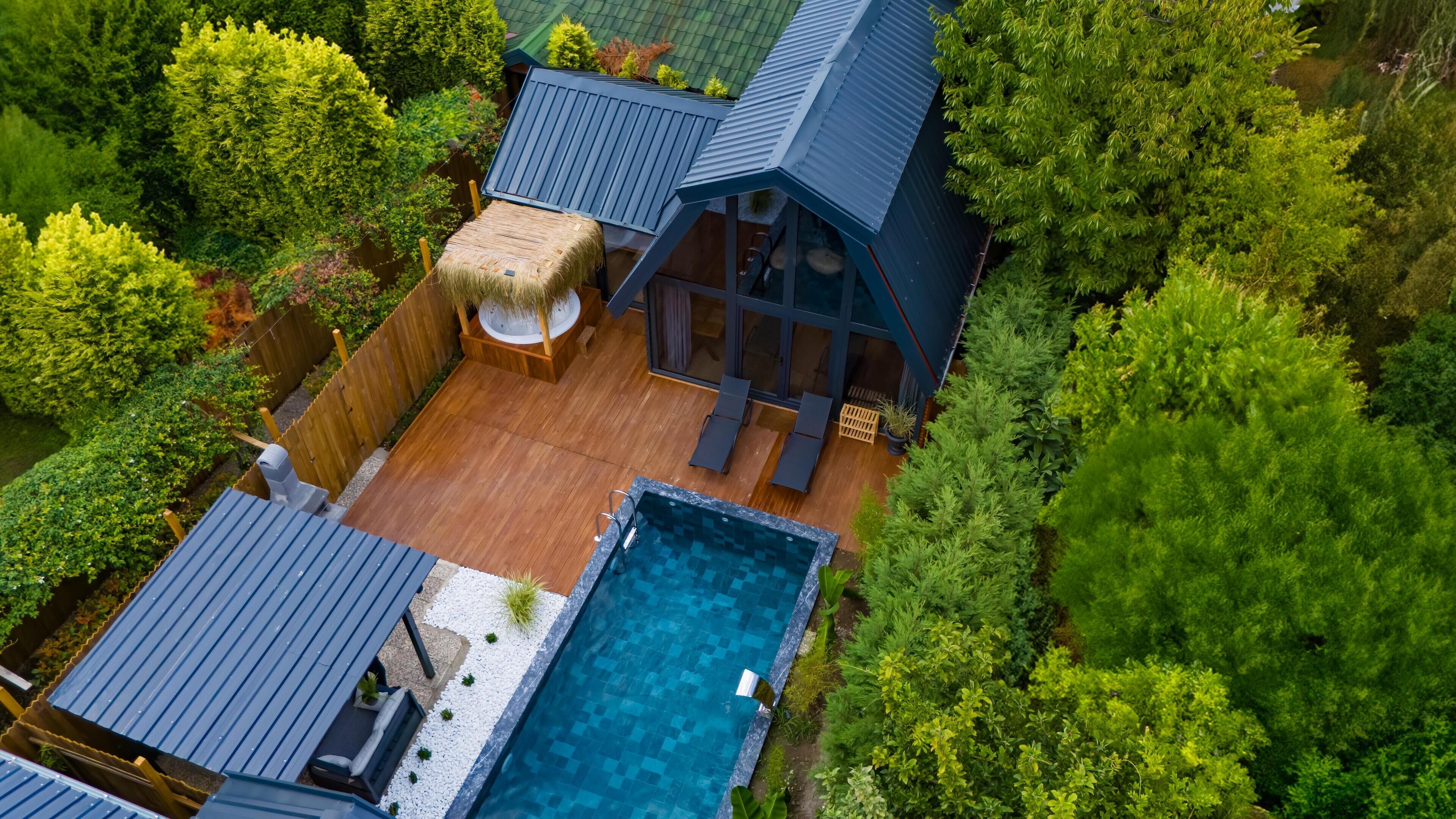 An aerial view of a modern house with a swimming pool, wooden deck, and lush greenery surrounding it.