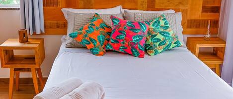A neatly made bed with a white sheet, multiple colorful pillows, and a rolled white towel on the side.