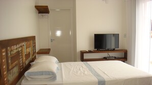 A neatly made bed with a wooden headboard, a bedside table with a book, and a TV on a wooden stand.