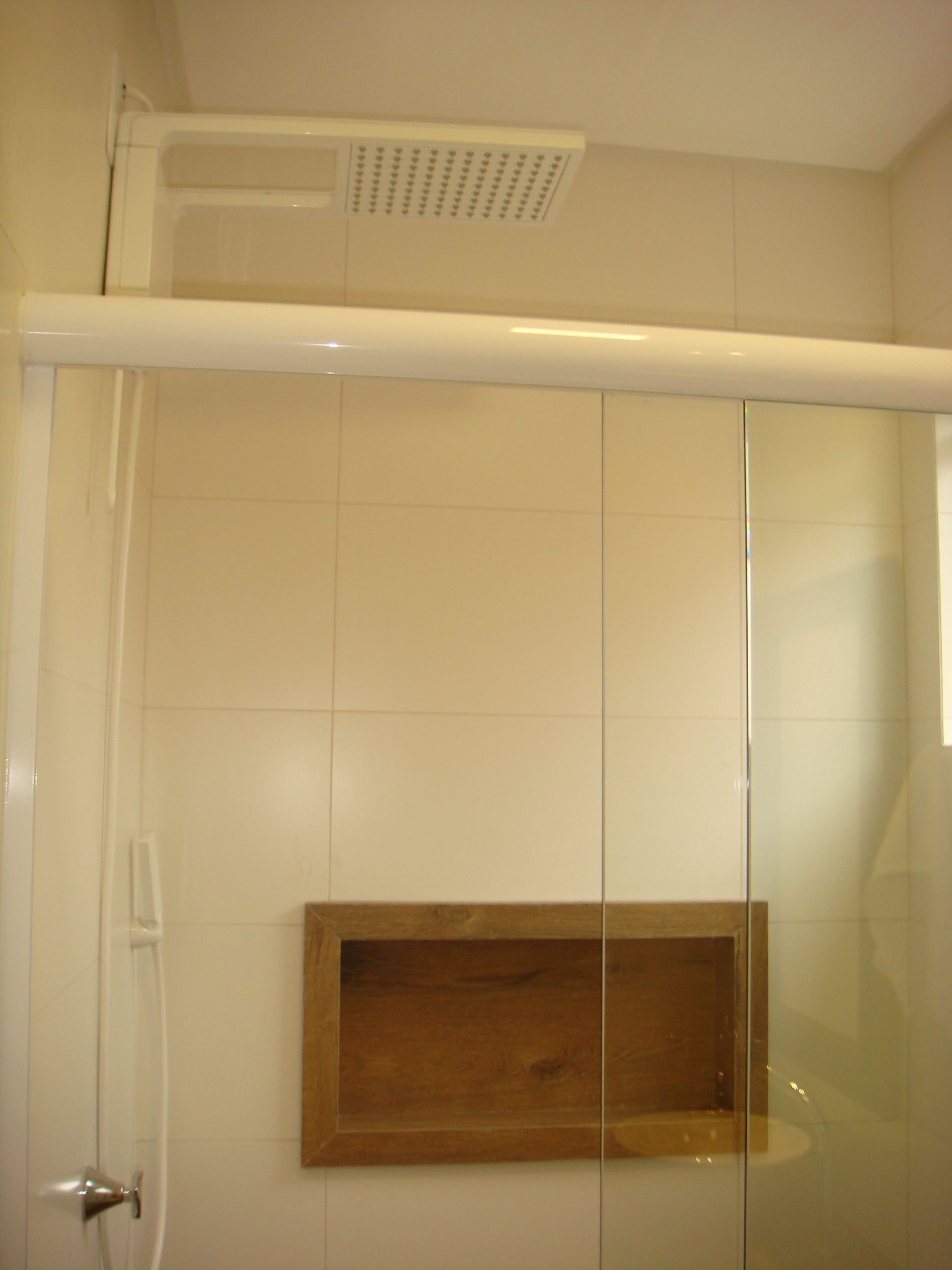 Box doccia con porta in vetro, ripiano in legno e bocchetta di ventilazione a soffitto.