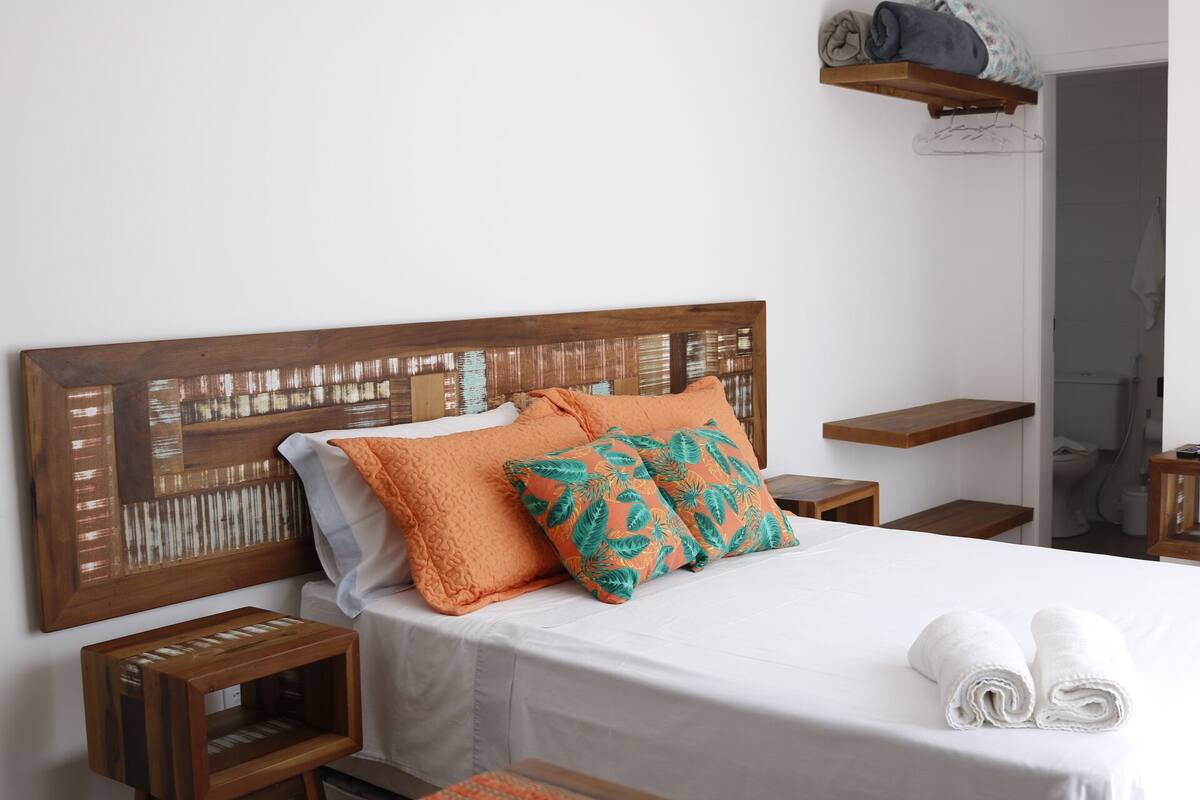 Una cama bien hecha con cabecera de madera, dos almohadas, una mesita de noche de madera y una toalla sobre la cama.