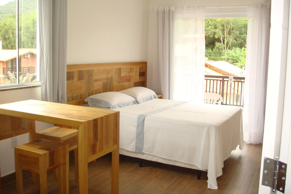 Un dormitorio con una cama y una mesa de madera, y un balcón con barandilla.