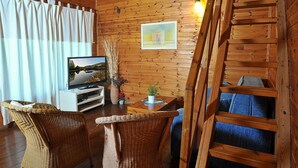 Una habitación acogedora con paredes de madera, televisor, sillas de mimbre, una mesita con una planta y un sofá azul.