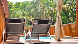 Dos sillones de descanso en una terraza de madera con una piscina al fondo.