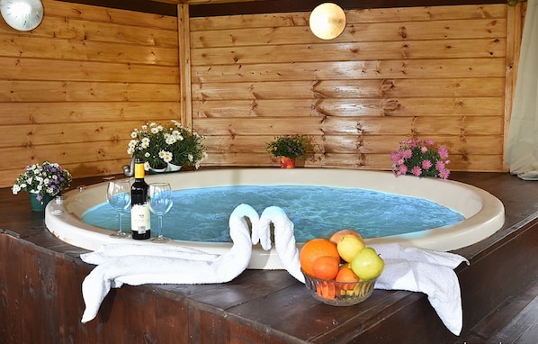 A hot tub with flowers, a bottle of wine, and fruit.