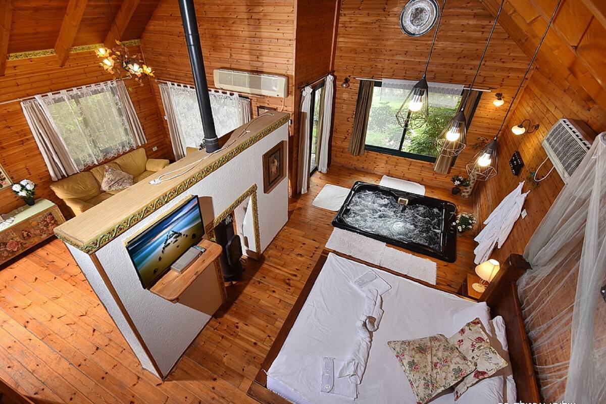 A cozy cabin with a wooden interior, a large bed, a hot tub, and a kitchen area.