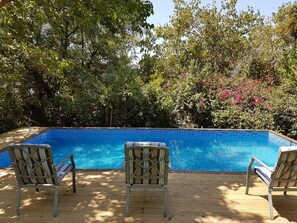 A rectangular swimming pool with a tiled edge, surrounded by a wooden deck. There are two lounge chairs facing the pool.