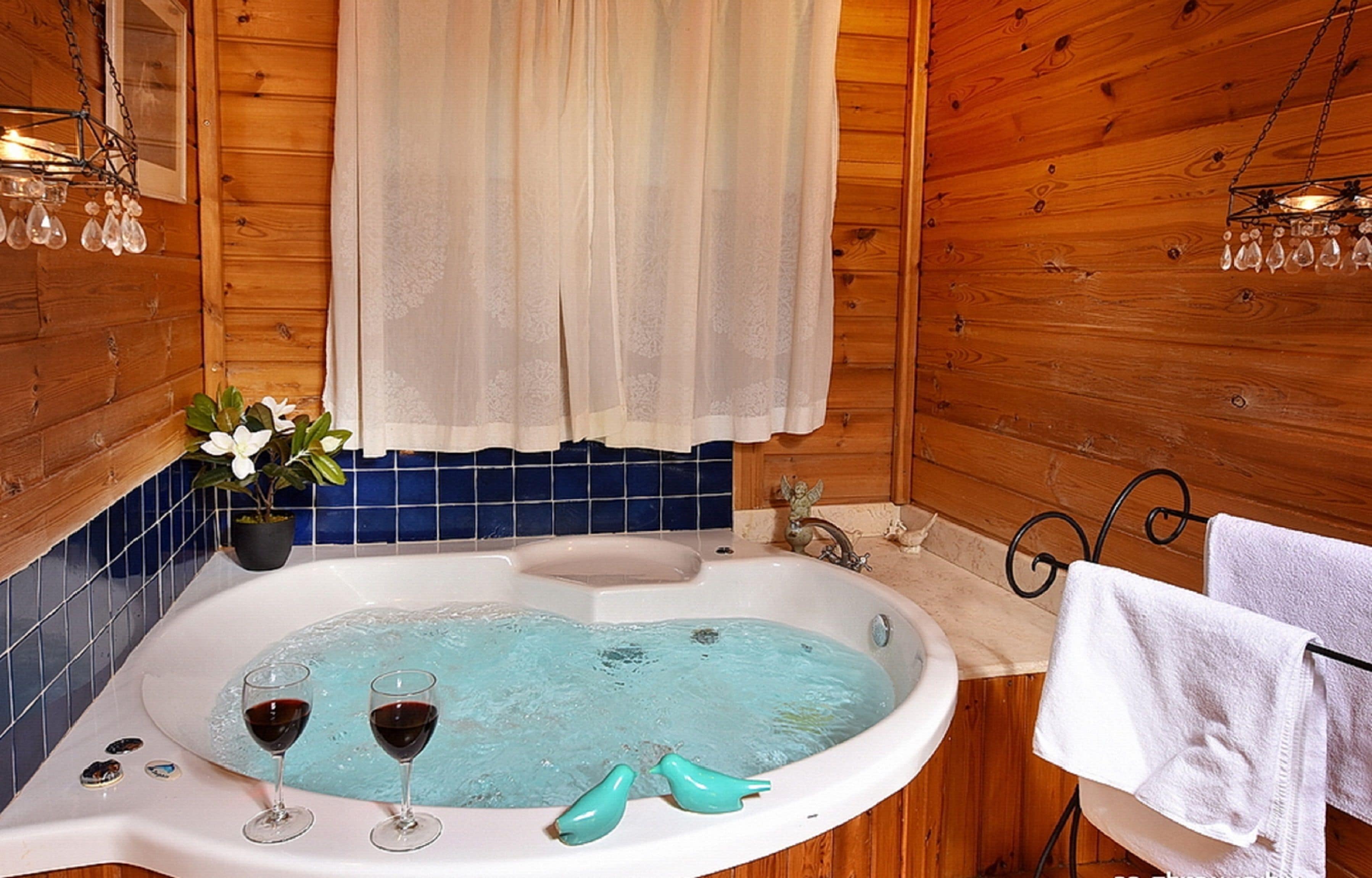 A wooden cabin bathroom with a bathtub, two wine glasses, a potted plant, and a towel rack.