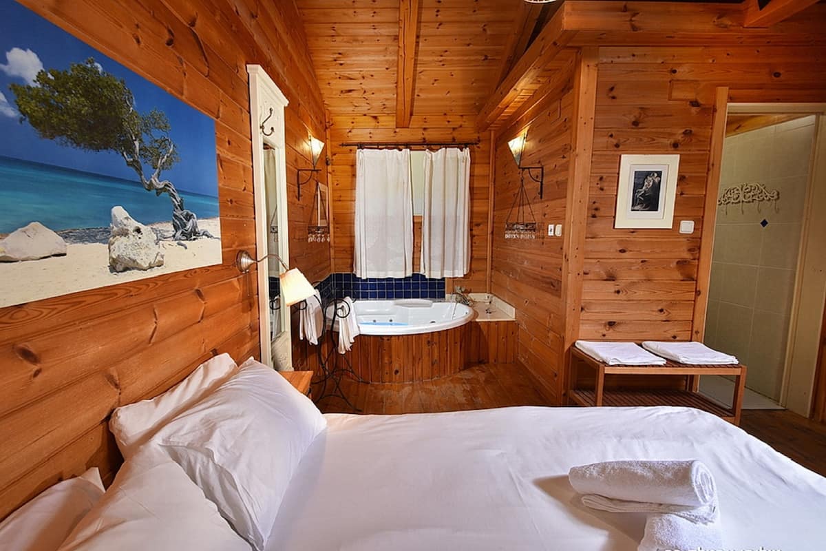 A wooden cabin room with a bed, a bathroom with a bathtub, and a painting of a beach scene.