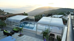 A rooftop pool area with glass enclosures, outdoor seating, and a view of distant hills. - Shlomo Cabins Boutique (Merom HaGalil)