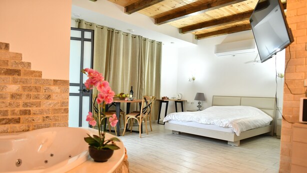 A bedroom with a bed, a desk, a chair, a TV, and a bathroom with a bathtub and a potted plant. - Shlomo Cabins Boutique (Merom HaGalil)