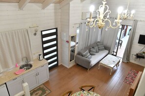 A compact living space with a kitchenette, a sofa, a dining table, and a chandelier. - Shlomo Cabins Boutique (Merom HaGalil)