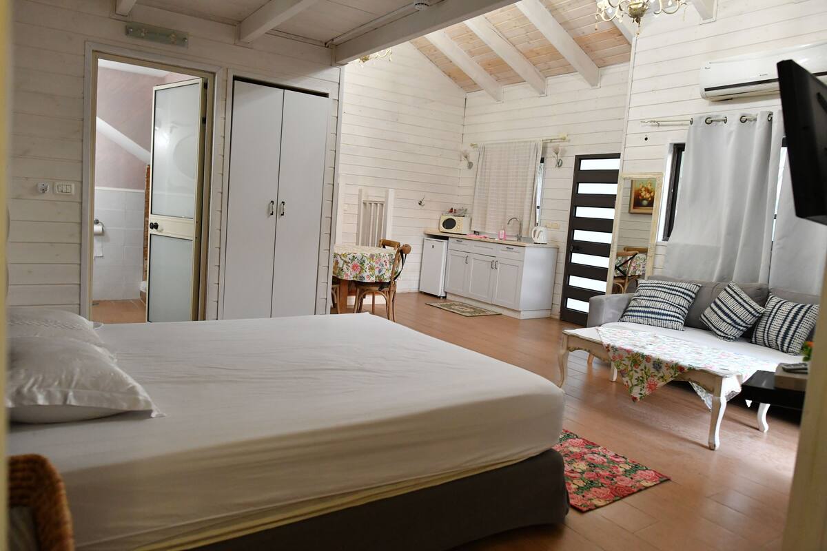 A bedroom with a bed, a desk, a chair, a sofa, and a small table with a floral tablecloth.