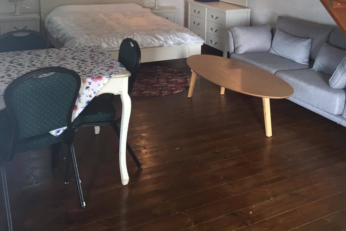 A compact room with a bed, a sofa, a small table, a chair, a desk, and a mirror.