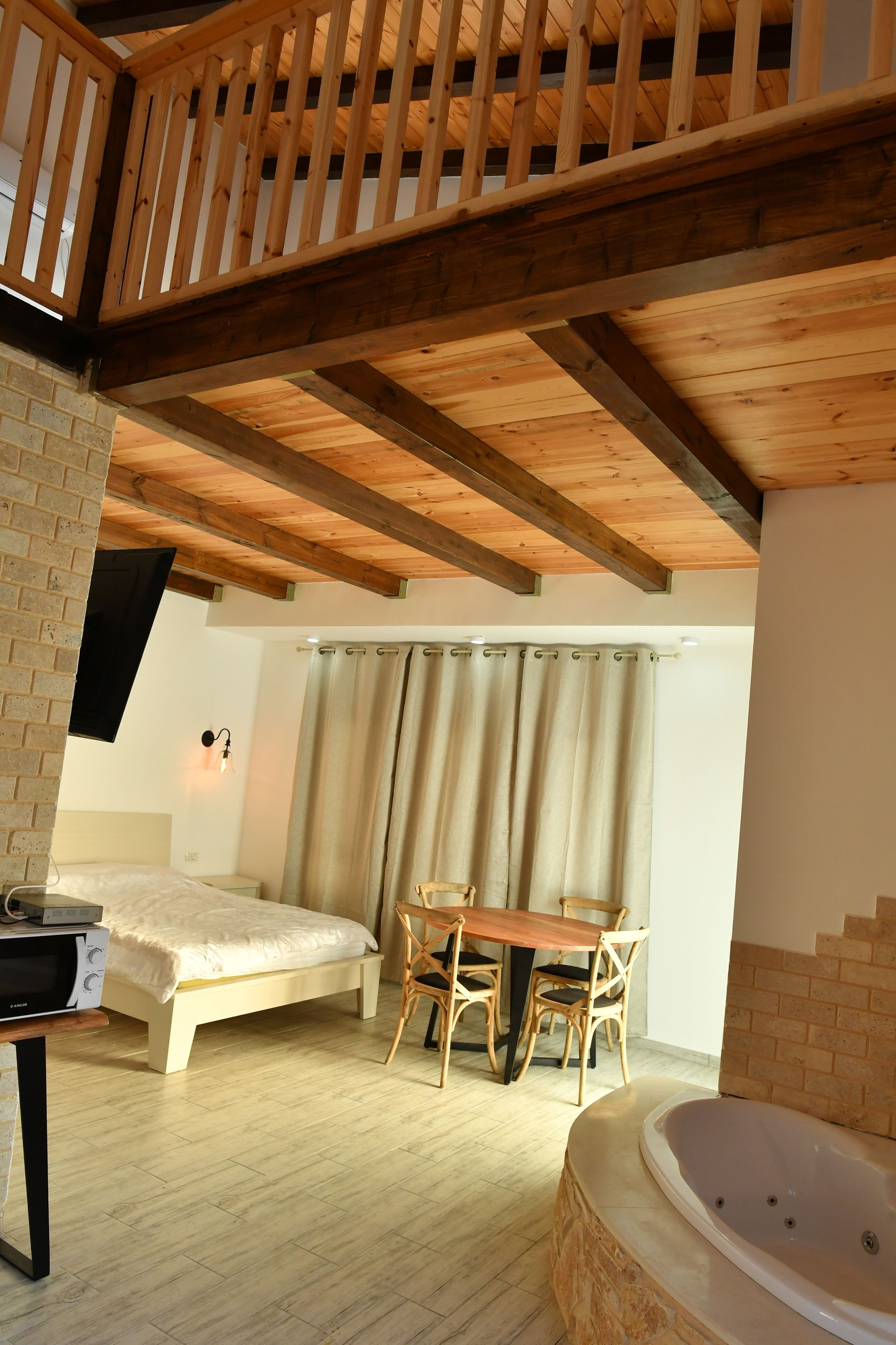 A bedroom with a wooden ceiling, a bed, a table with chairs, a TV, and a bathtub.
