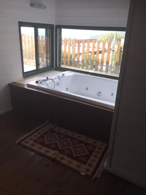 A bathroom with a large bathtub, a wooden floor, and a patterned rug. - Shlomo Cabins Boutique (Merom HaGalil)
