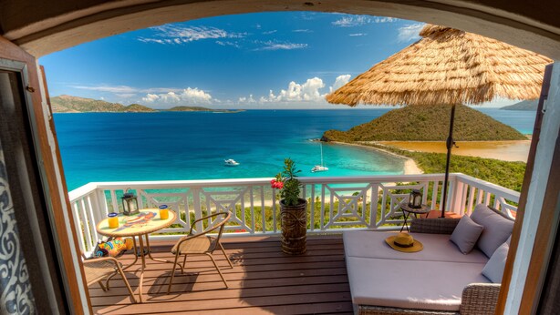 Una terraza con un sofá de mimbre, una mesa y sillas, con vista al mar turquesa y a la playa.
