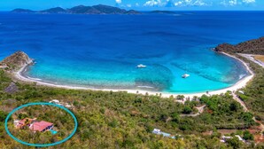 Vista aérea de una isla tropical con mar azul cristalino, una playa de arena y un pequeño edificio rodeado de vegetación.