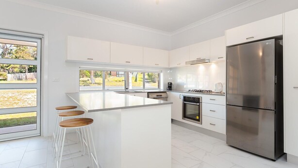 A modern kitchen with white cabinetry, a stainless steel refrigerator, a built-in oven, and a large island with bar stools.
