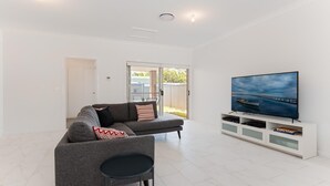A modern living room with a grey sofa, a small black table, and a large flat-screen TV on a white stand.