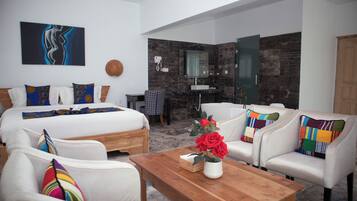 Ein Hotelzimmer mit einem großen Bett, zwei weißen Sessel, einem Holztisch mit einer Rosenvase, einem Badezimmer mit einer Glasdusche und einer Marmorwand.