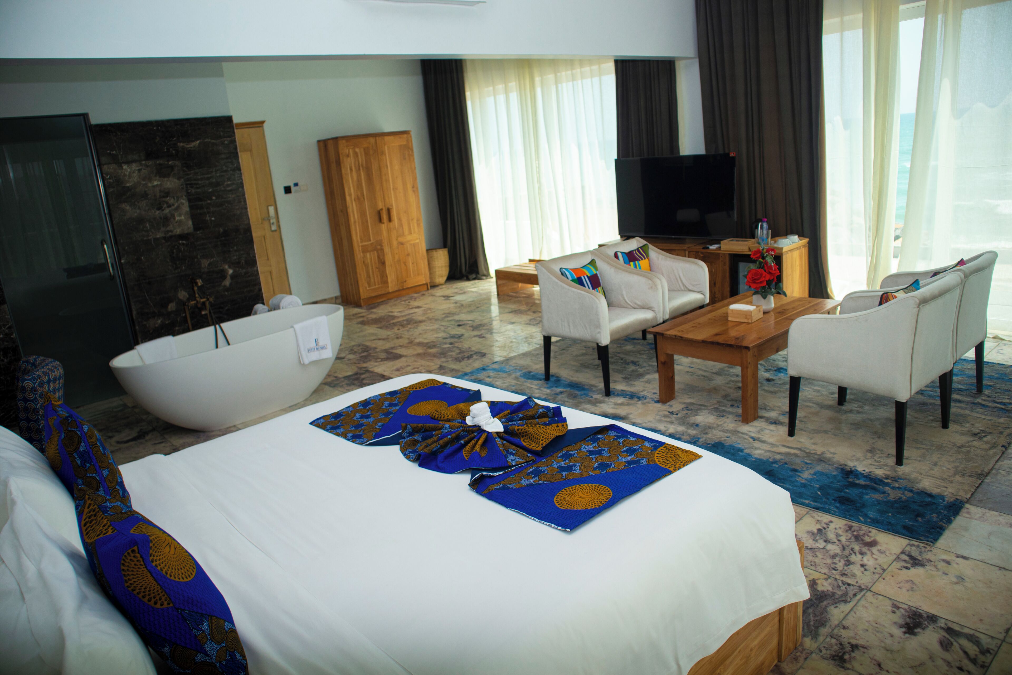 Habitación de hotel con cama, sofá, mesa de centro, televisor y vista al océano.