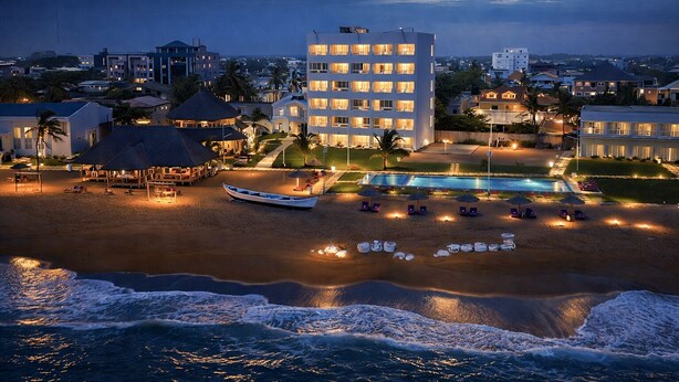 Un hotel frente a la playa con piscina, sillas de playa y sombrillas.
