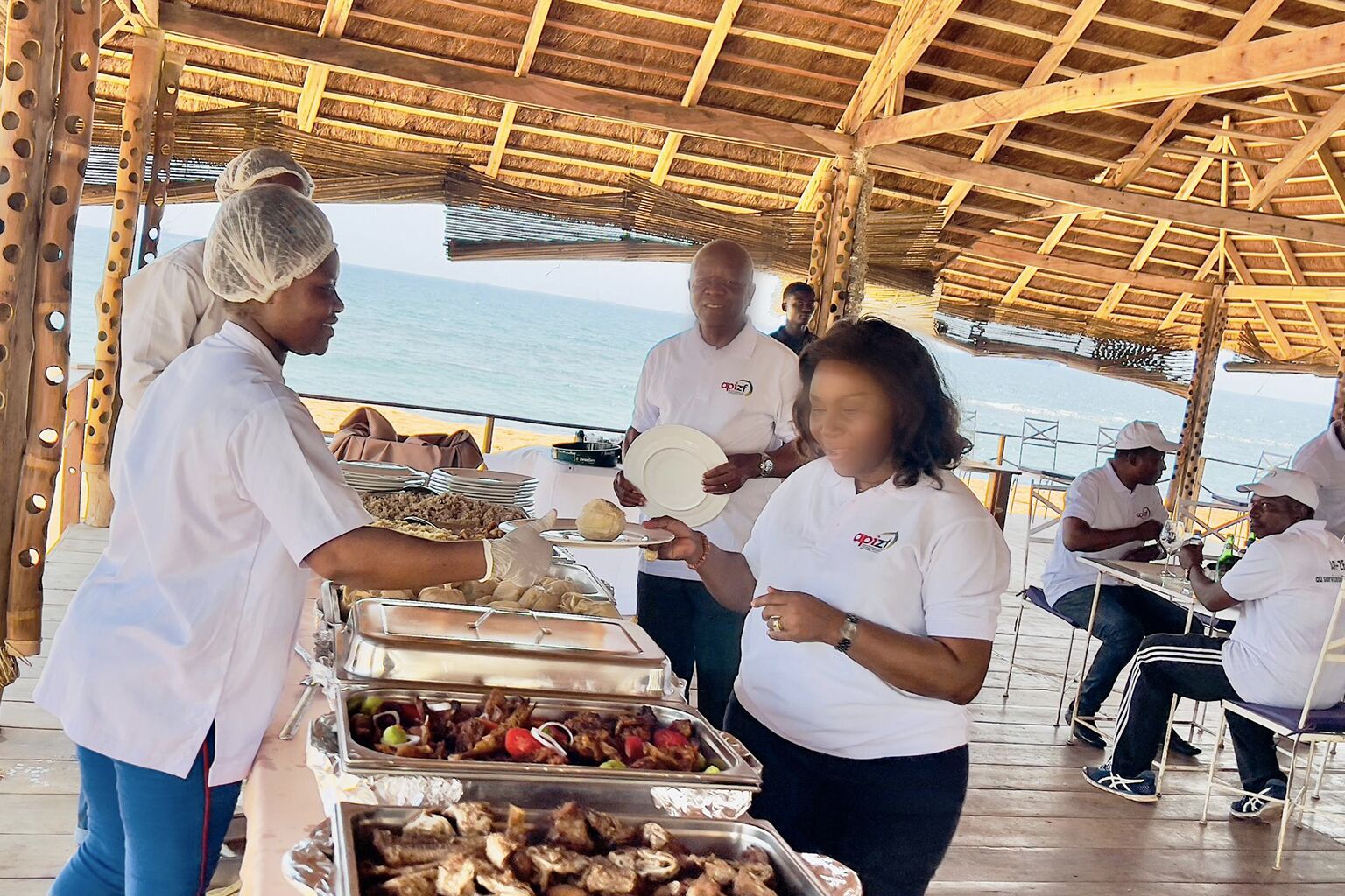 A buffet setup with various food items and people serving and eating.