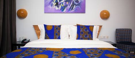 A hotel room with a bed, a painting on the wall, two wall sconces, a chair, and a telephone on a nightstand.