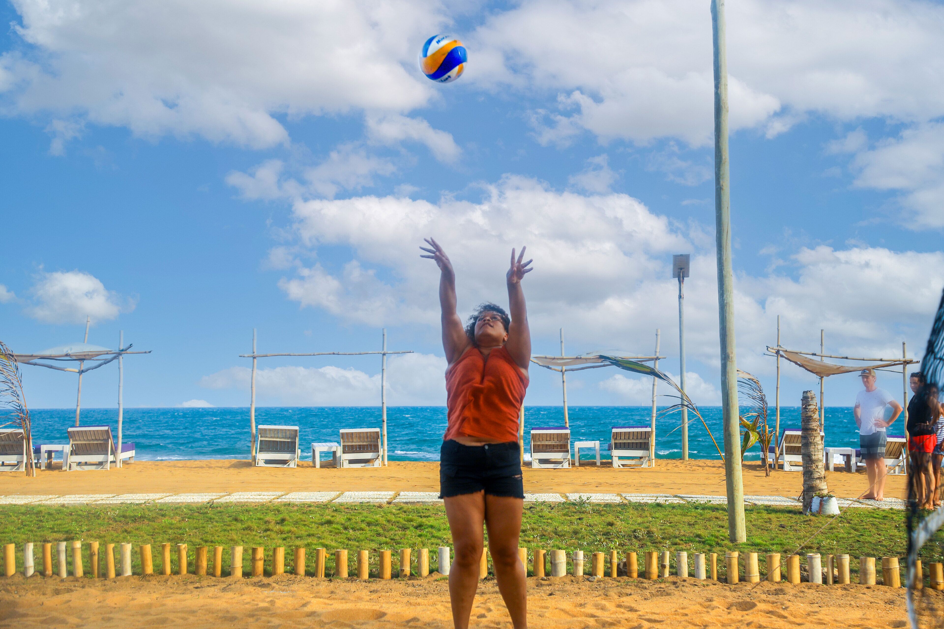 A beach volleyball player in mid-action with beach chairs and umbrellas in the background.