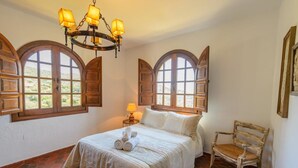 Ein Schlafzimmer mit einem Bett, einem Sessel und zwei Fenstern mit Rollläden.