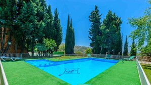 Ein rechteckiger Swimmingpool mit Sprungbrett, umgeben von einem weißen Zaun und grünem Kunstrasen.