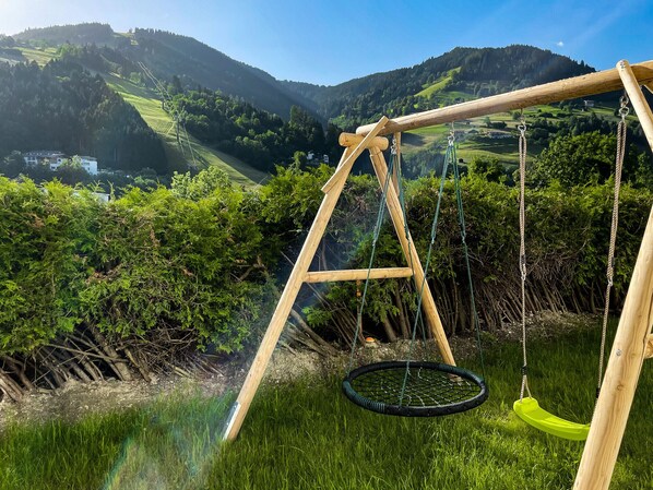 A wooden swing set with a green seat, set against a backdrop of lush green hills and a clear sky. - Tevini Alpine Apartments - Schmittenblick, balcony (Zell am See)