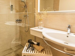 Une salle de bain avec une douche à parois de verre, un lavabo blanc et un porte-serviettes avec une serviette et un sèche-cheveux.